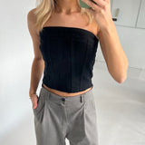 En kvinde tager et spejlselfie med en grøn telefon. Hun er iført en sort, stropløs top og grå bukser i et hvidt rum.