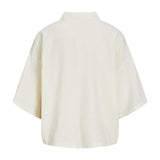 Skjorte med korte ærmer hænger stille, set bagfra. Den er ensfarvet og har et klassisk, løstsiddende design i en lys farve. Baggrunden er neutral.