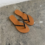Et par brune flip-flops ligger stille på en grå, rå betonoverflade i et sparsomt belyst rum.