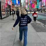 En person med en "Los Angeles"-trøje går på en travl byfortov om dagen. Omkring ses andre fodgængere, skyskrabere og store reklameskærme.