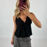 En person tager en selfie med en mobiltelefon iført en sort top og grå bukser. Baggrunden er hvid, hvilket fremhæver tøjet og skaber en minimalistisk kontekst.