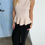 En kvinde står iført en lys top med peplum og sorte bukser, med en blå dør i baggrunden.
