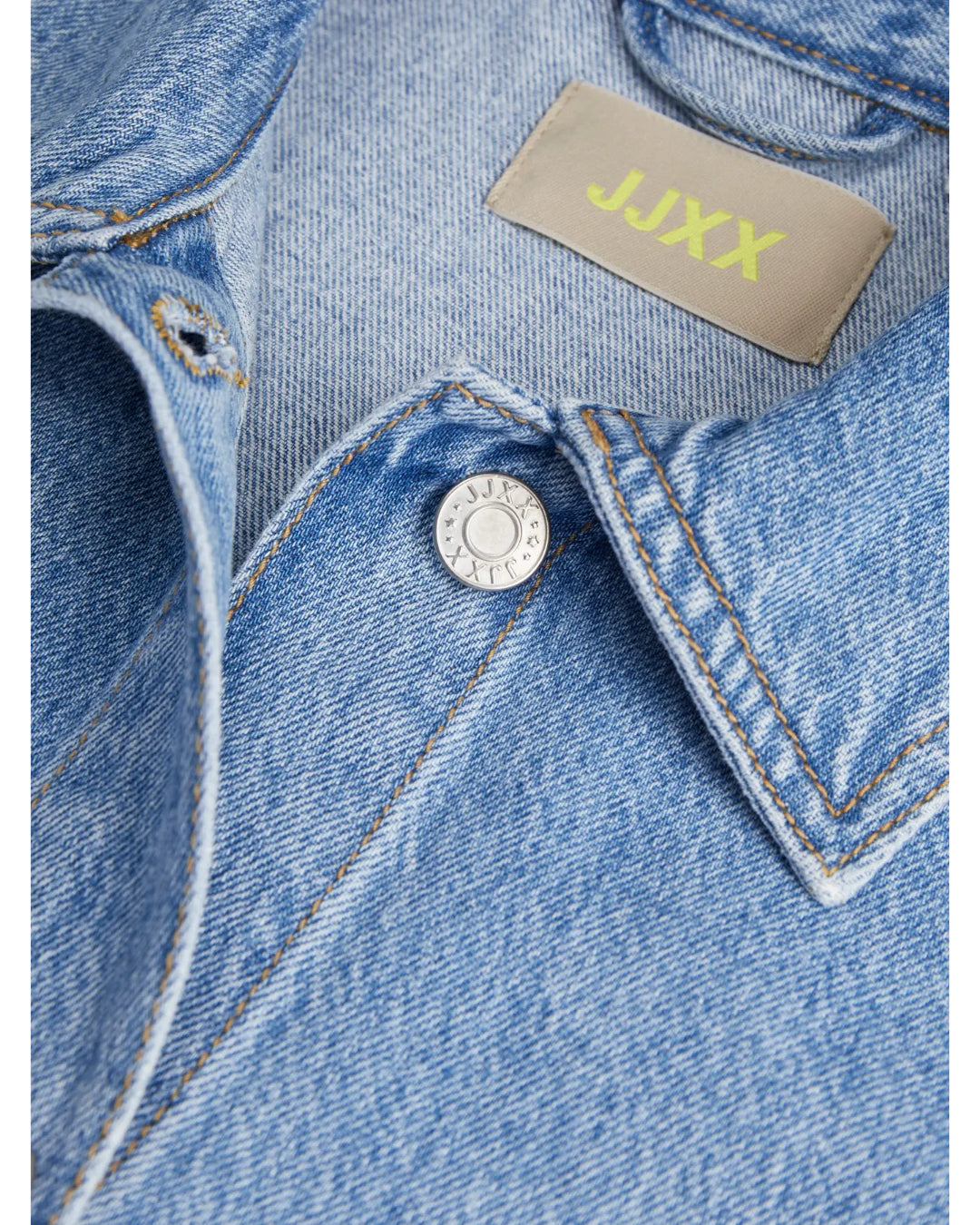 Denimjakke med syning ses tæt på. En sølvknap med teksten "JACK&JONES" er synlig. Mærket "JJXX" i gul står ved kraven.