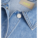 Denimjakke med syning ses tæt på. En sølvknap med teksten "JACK&JONES" er synlig. Mærket "JJXX" i gul står ved kraven.
