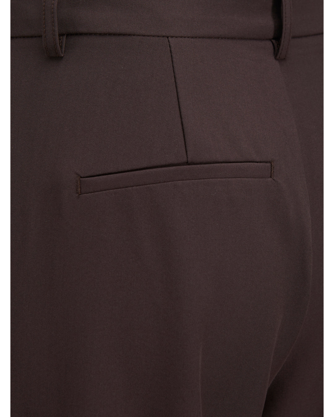 Baglommen på et par mørkebrune bukser vises med en enkelt lommesøm. Bukserne har et minimalistisk design med én bæltestrop øverst i synsfeltet.