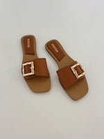 To brune sandaler med store, firkantede spænder ligger på en flad, hvid overflade. Mærket "moow" er trykt indeni sålerne.
