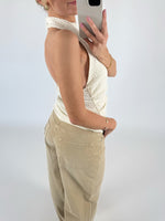 En person iført en hvid top og beige bukser tager et spejlbillede med en smartphone i en minimalistisk, hvid baggrund.