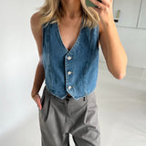 Denimvest bæres af en person, der tager et spejlbillede, handske i grå bukser. Personen står i et lyst rum med hvide vægge.