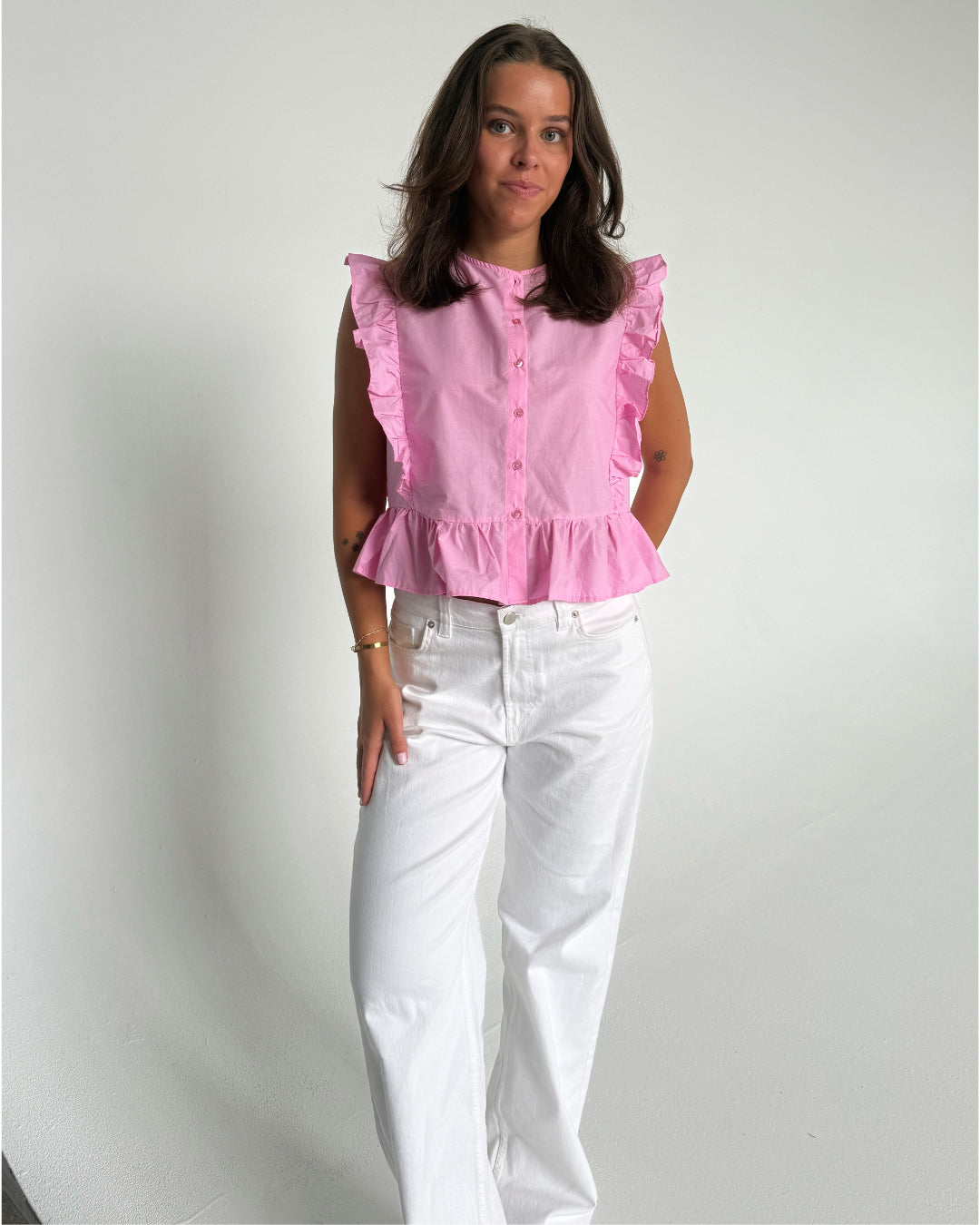 Modelfoto af pige som bærer Hope Cilie top i lyserød, samt et par hvide Nanna jeans. Alt fra By Sofie Sønderby