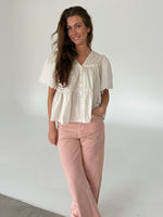Modelfoto af pige som bærer creme-farvet HOPE top med v-hals og lyserøde jeans. Alt er fra BySofieSønderby