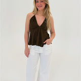 Kvinde i brun top og hvide bukser står smilende med en hånd i lommen. Baggrunden er neutral og hvid.