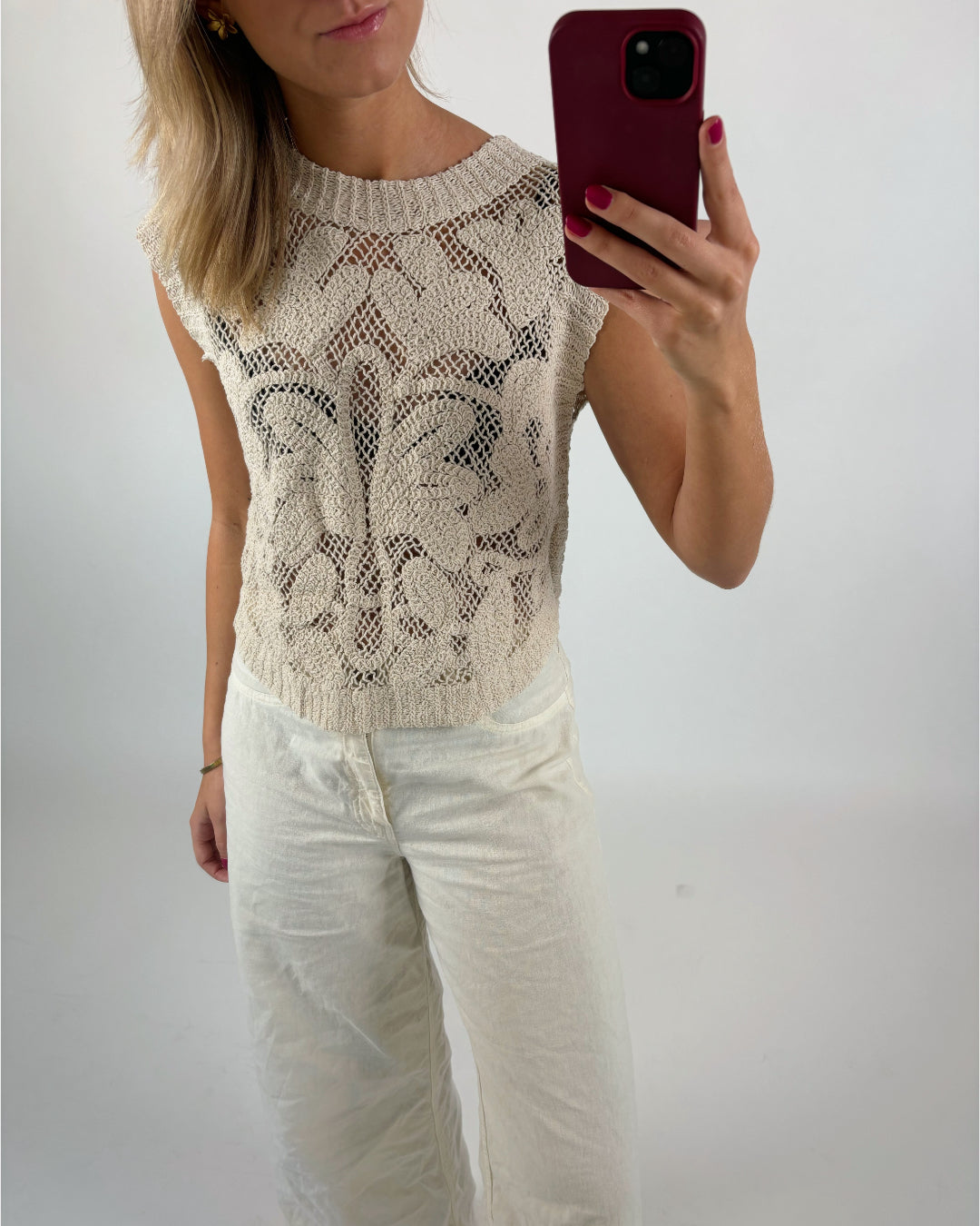 En person i en lysebrun, mønstret striktop og hvide bukser tager et spejlbillede med en smartphone, i et enkelt, lyst rum.