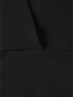 Sort stof ligger fladt med en tydelig syning på tværs midt i billedet og skaber en skarp kontrast. Baggrunden er ensfarvet og enkel.