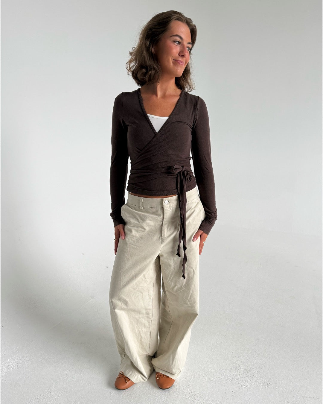 Modelfoto af pige i brun Luna wrapbluse og beige bukser. Fra BySofieSønderby