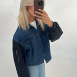 Kvinne i cowboyjakke tager et selfie, står i et neutralt rum. Hun har lyst hår og en mobiltelefon dækker hendes ansigt delvist. Ingen yderligere tekst eller detaljer i baggrunden.