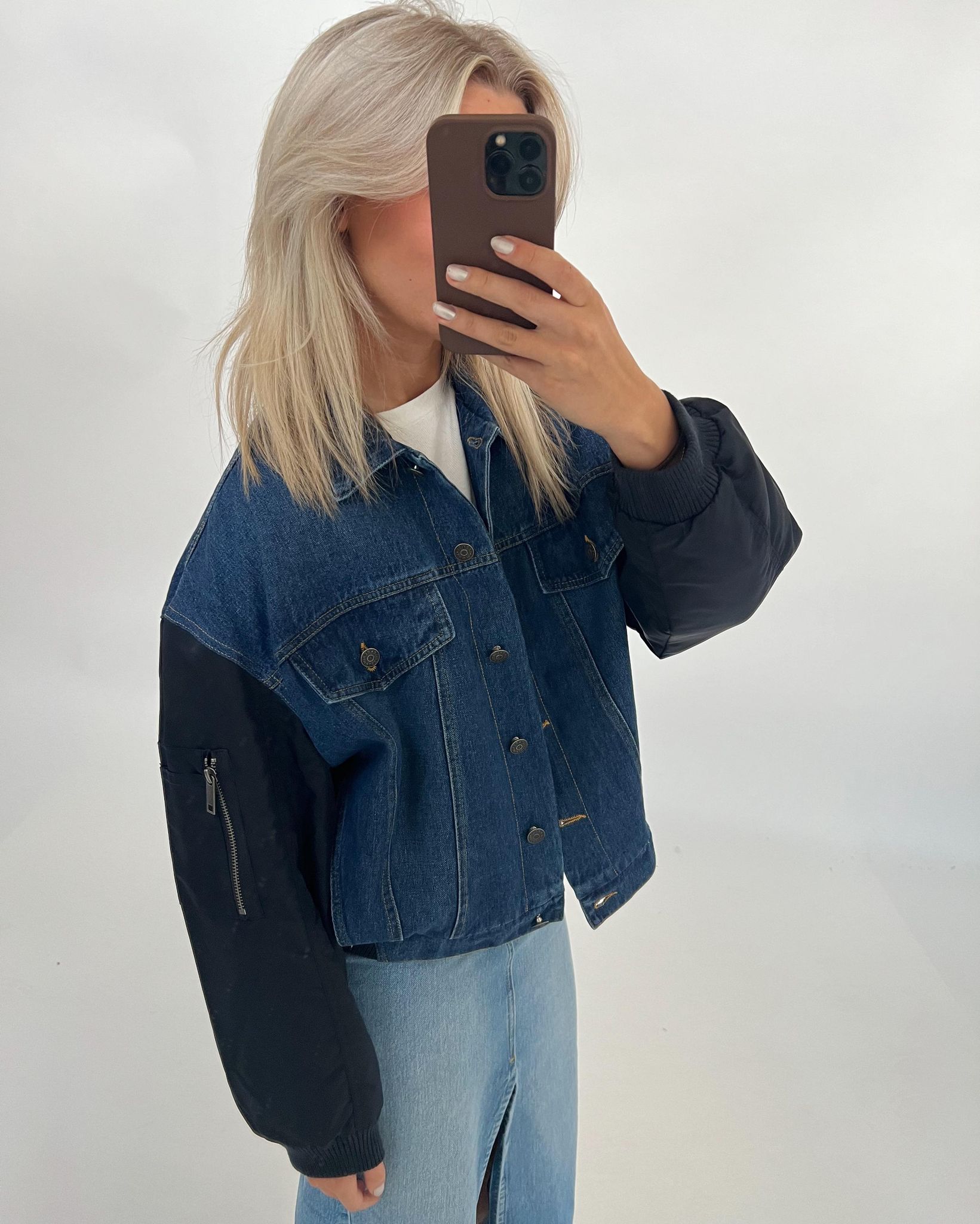 Kvinne i cowboyjakke tager et selfie, står i et neutralt rum. Hun har lyst hår og en mobiltelefon dækker hendes ansigt delvist. Ingen yderligere tekst eller detaljer i baggrunden.