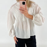 En person i en hvid bluse tager et billede med en mobiltelefon med lyserødt cover i et minimalistisk, lyst rum.