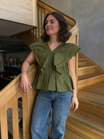 Kvinde står på trappe, iført en grøn bluse og blå jeans. Hun hviler hånden på gelænderet i en moderne, træinteriørindretning med dæmpet belysning.