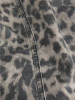 Grå og sort leopardmønstret stof ligger foldet med en synlig søm. Stoffet ser jævnt ud, hvilket tyder på tøj eller tekstil i blødt materiale.