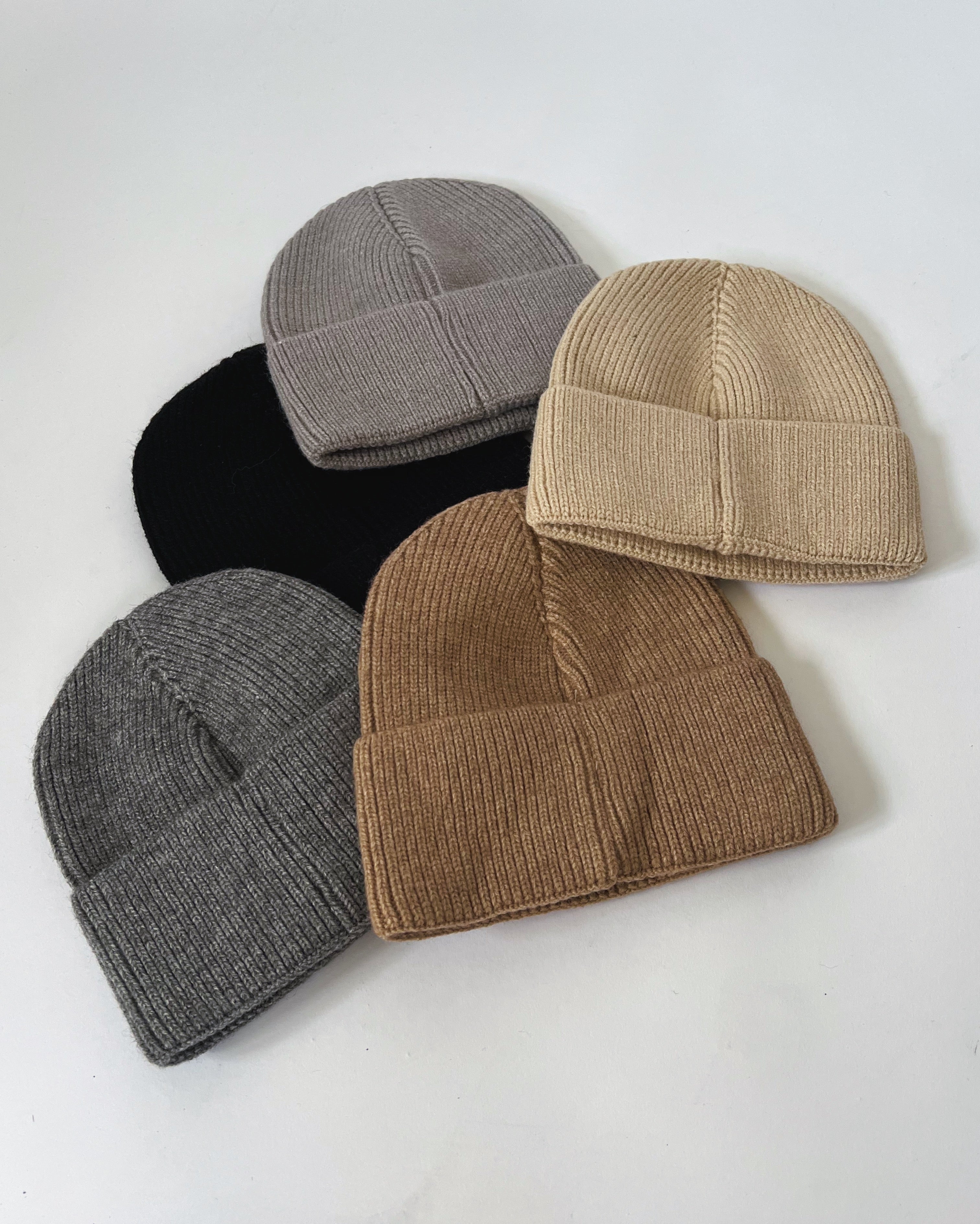 Fem strikhuer, i grå, beige, sort og brun farver, ligger roligt arrangeret på en hvid overflade.