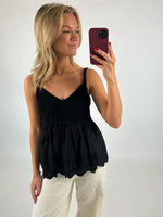 Kvinde iført sort top tager et selfie med en rød mobiltelefon, mens hun står imod en hvid baggrund i et fotostudielignende miljø.