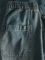 Baglomme af denimshorts med elastisk talje ses tæt på, viser denimvævningens blå farve og robuste syninger i et enkelt, afslappet design.