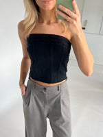 En kvinde tager et spejlselfie med en grøn telefon. Hun er iført en sort, stropløs top og grå bukser i et hvidt rum.