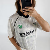 En kvinde tager et billede af sig selv med en telefon foran ansigtet. Hun er iført en retro fodboldtrøje med stjernemønster og teksten "SPORTS CHALLENGE THE BEST IS YET TO COME".