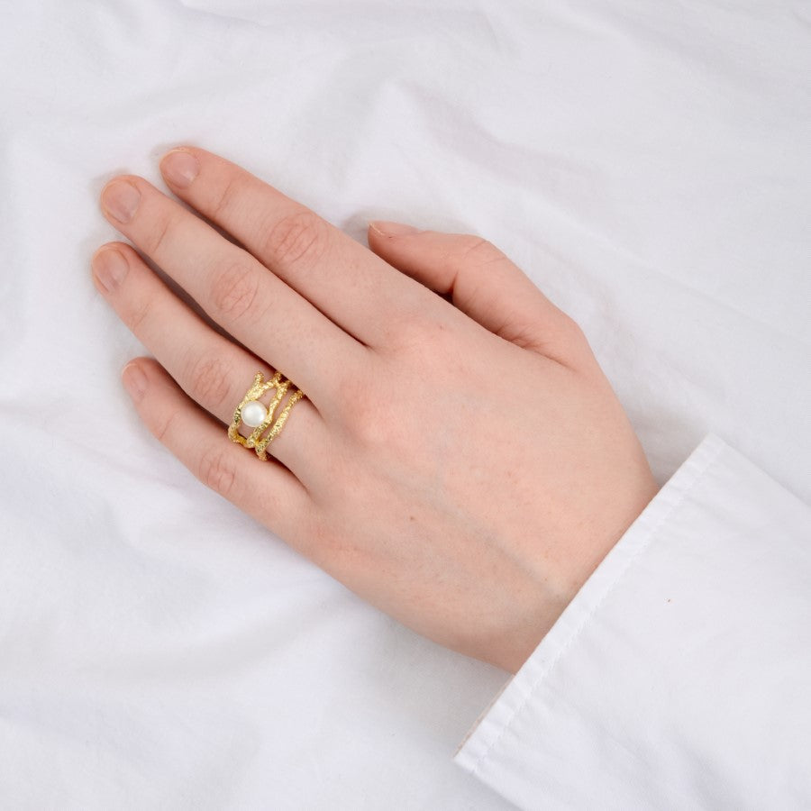 Hånd med en gylden ring med en perle bæres; baggrunden er en hvid klud.
