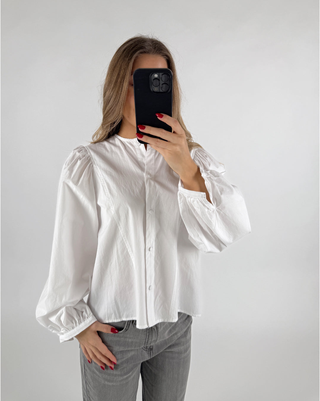 En person i en hvid skjorte tager et selfie med en sort mobiltelefon. Baggrunden er en neutral væg.