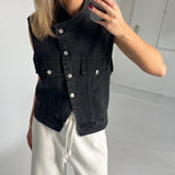 En person iført en sort denimvest med knapper tager et spejlfoto. Personen har hvide bukser på og står i et lyst rum.