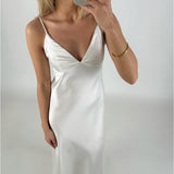 En person iført en hvid satin kjole tager et selfie med en smartphone i et lyst rum. Personen bærer et gyldent armbånd på højre håndled.