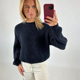 Kvinde tager et spejlbillede med mobiltelefon. Hun har en mørk sweater og lyse bukser på. Baggrunden er en simpel, lys væg.