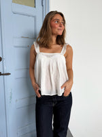 Modelfoto af pige som bærer en Amona top i hvid, samt et par mørkeblå jeans. Alt fra By Sofie Sønderby