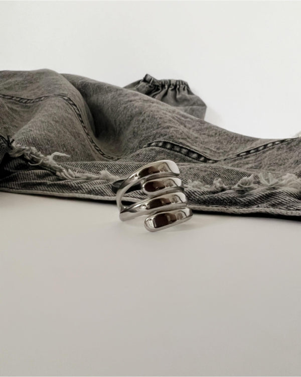En blank, sølvfarvet ring ligger på en glat overflade ved siden af et par grå, frynsede jeans.