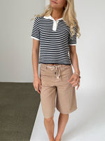 En person står iført en sort- og hvidstribet trøje og beige shorts. De står på et gulv med to forskellige farver, brun og hvid, i en enkel, lys tekstur.