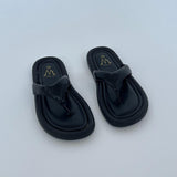 Sorte sandaler ligger stille på en lys baggrund. Sandalerne har en skinnende finish med logoet "Me CINK ME" trykt i guld på indersålerne.