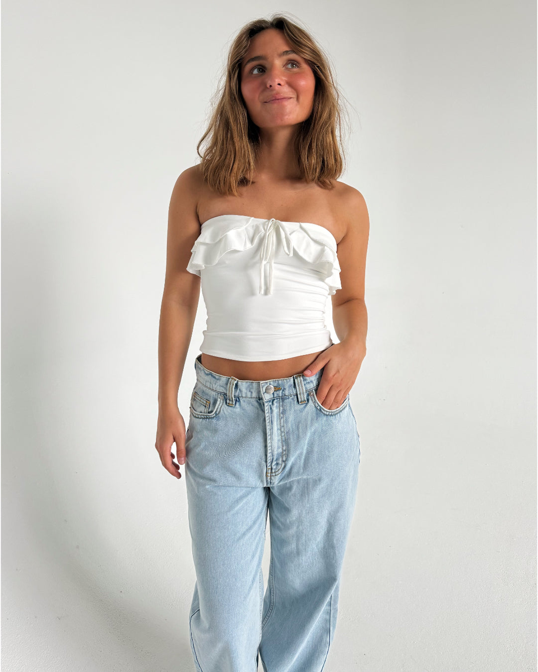 Modelfoto af pige der bærer en hvid stropløs Bonnie top, samt lyseblå Nanna jeans. Alt fra BySofieSønderby