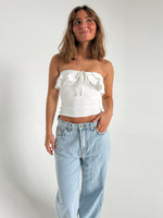 Modelfoto af pige der bærer en hvid stropløs Bonnie top, samt lyseblå Nanna jeans. Alt fra BySofieSønderby