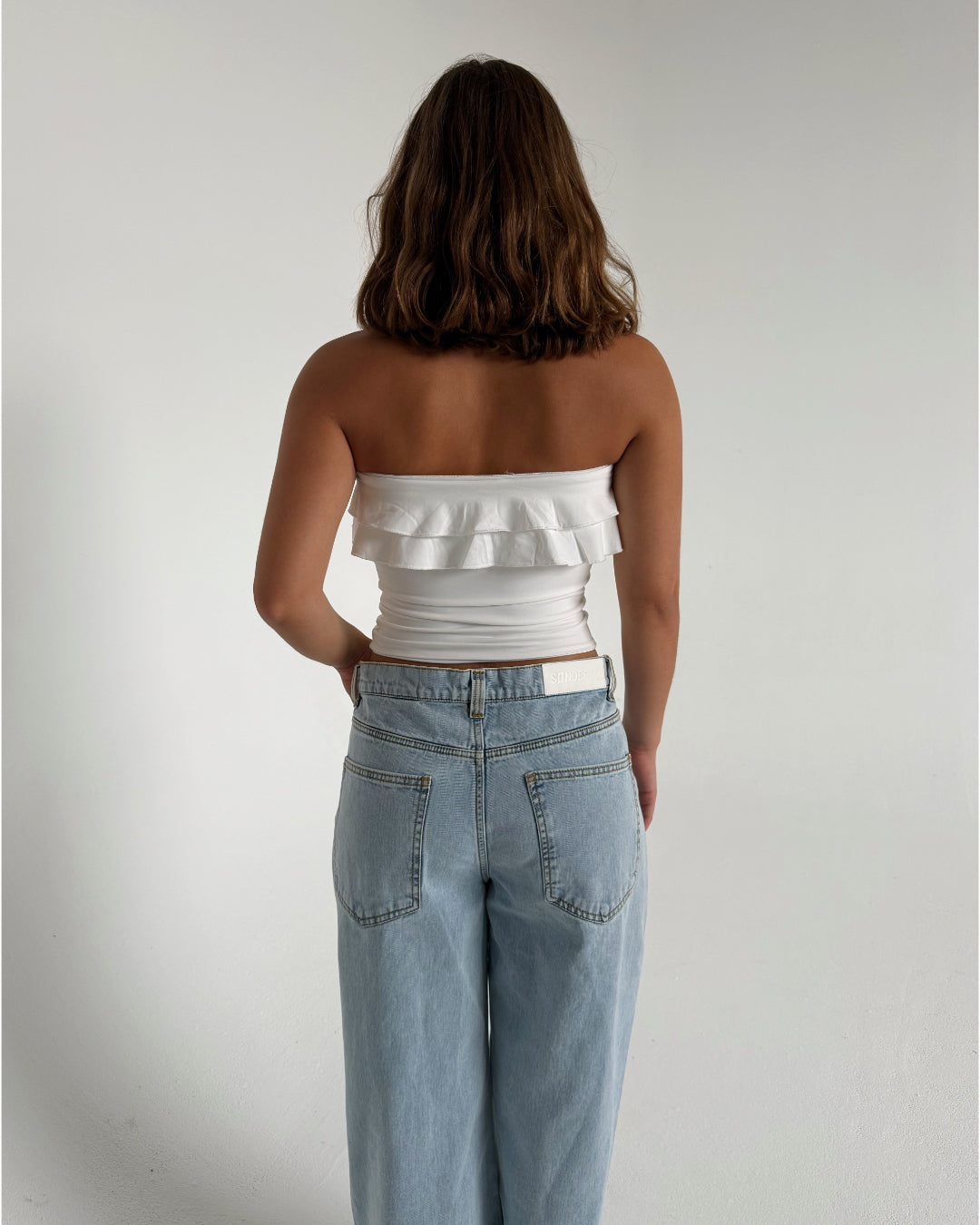 Modelfoto af pige der bærer en hvid stropløs Bonnie top, samt lyseblå Nanna jeans. Alt fra BySofieSønderby