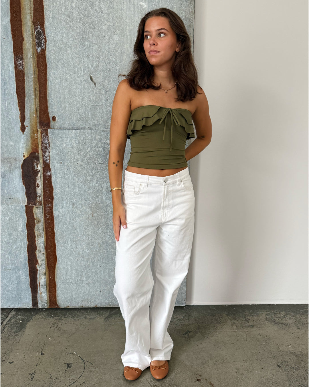Modelfoto af pige der bærer en kaki farvet stropløs Bonnie top, samt hvide Nanna jeans. Alt fra BySofieSønderby