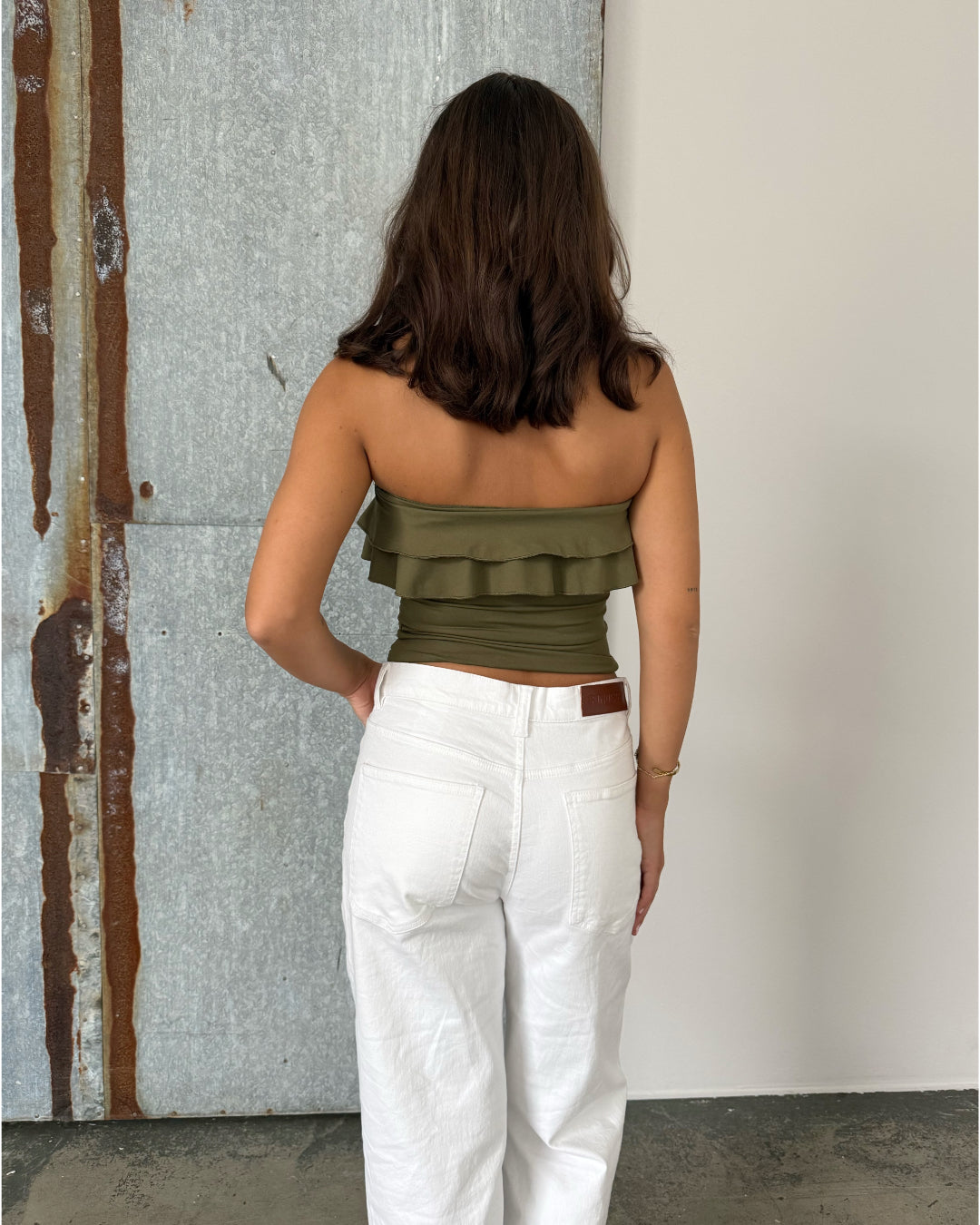 Modelfoto af pige der bærer en kaki farvet stropløs Bonnie top, samt hvide Nanna jeans. Alt fra BySofieSønderby