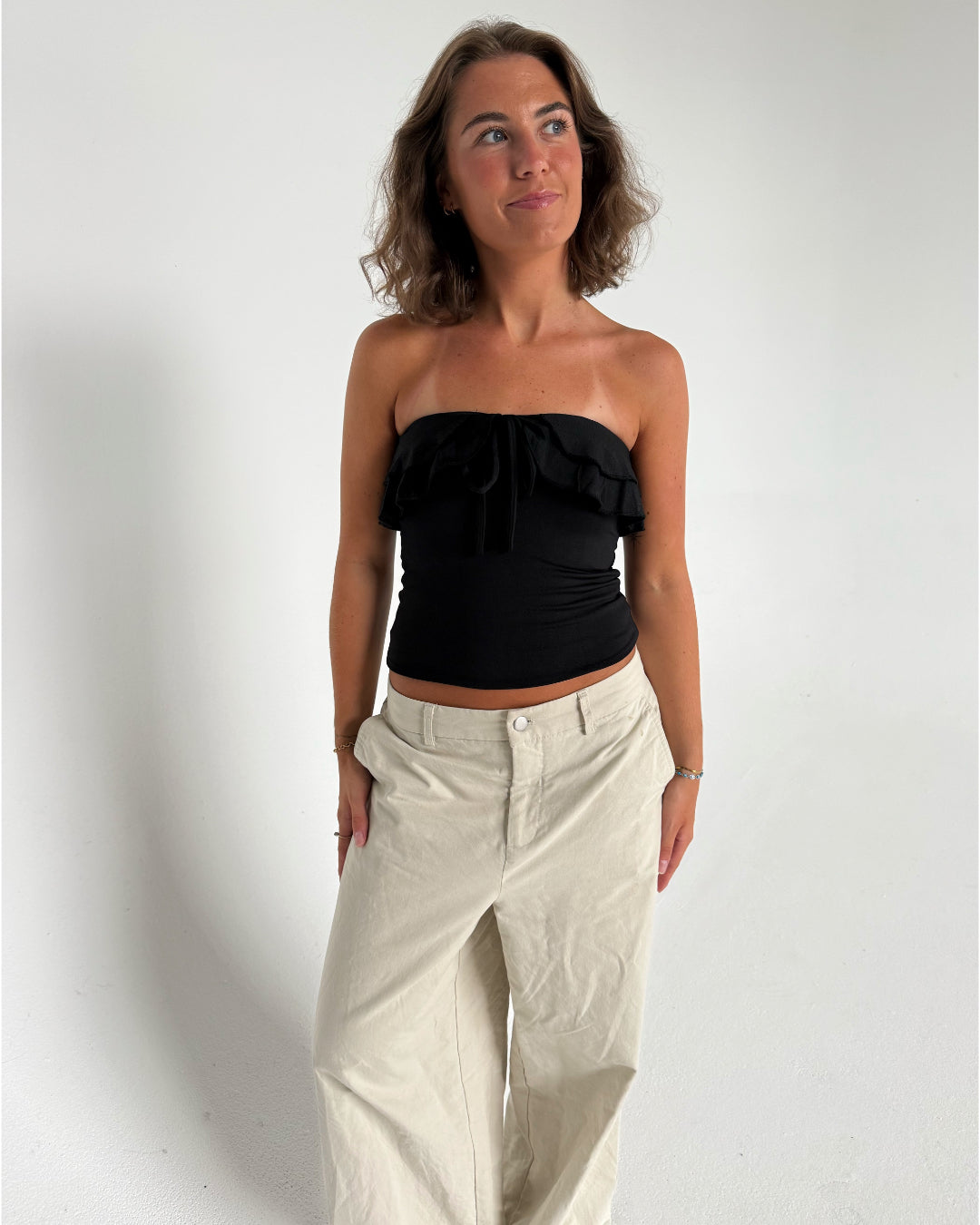 Modelfoto af pige der bærer en sort stropløs Bonnie top, samt beigefarvede bukser. Alt fra BySofieSønderby