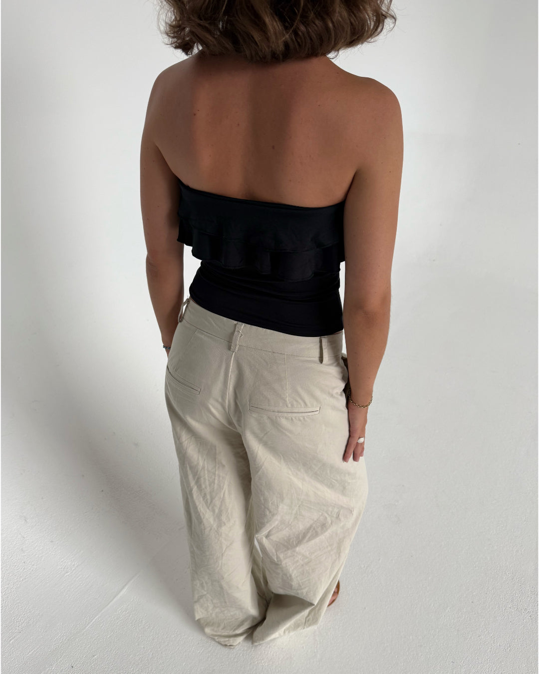 Modelfoto af pige der bærer en sort stropløs Bonnie top, samt beigefarvede bukser. Alt fra BySofieSønderby