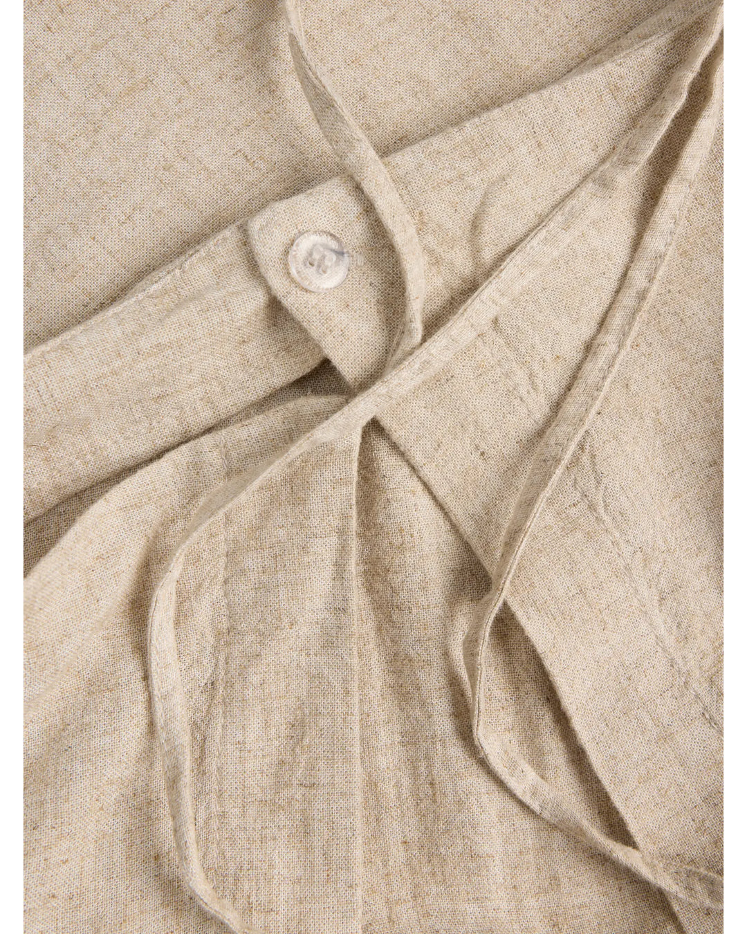 Lys beige stof med synlig knap og lapper, der lægges over hinanden. Stoffet ligger fladt uden specifik kontekst.