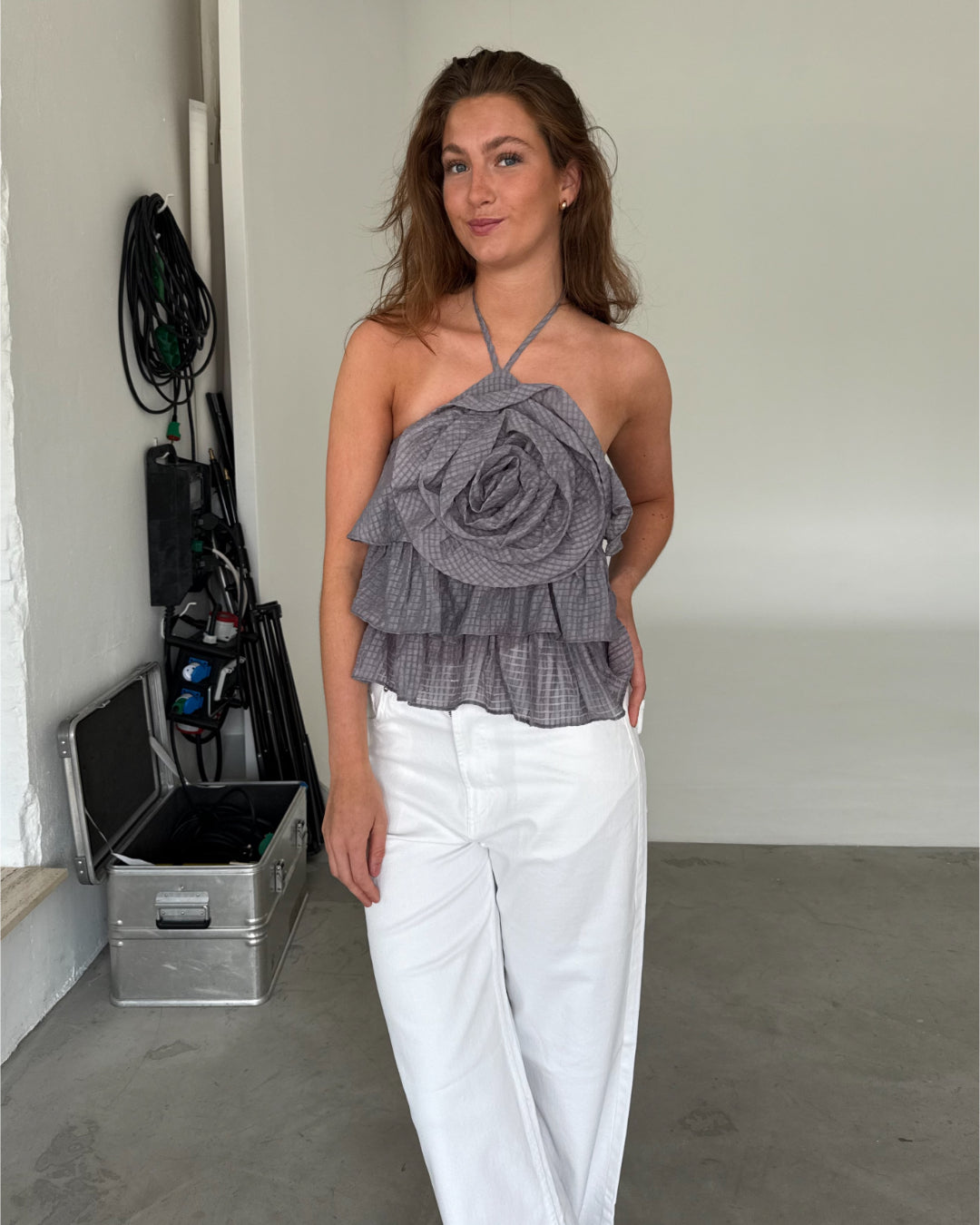 Modelfoto af pige som bærer en grå BRITNEY halterneck top med blomst på bryst, samt hvide jeans. Alt er fra BySofieSønderby