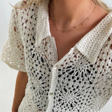 En hvid hæklet cardigan bæres af en person. Trøjen er knapper foran og har et blomstermønster. Personen har en guldhalskæde på, i et lyst indendørs miljø.