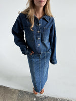 Modelfoto af pige som bærer en blå Cana denim jakke, samt Cana denim nederdel og sorte Carmen sandaler. Alt fra By Sofie Sønderby