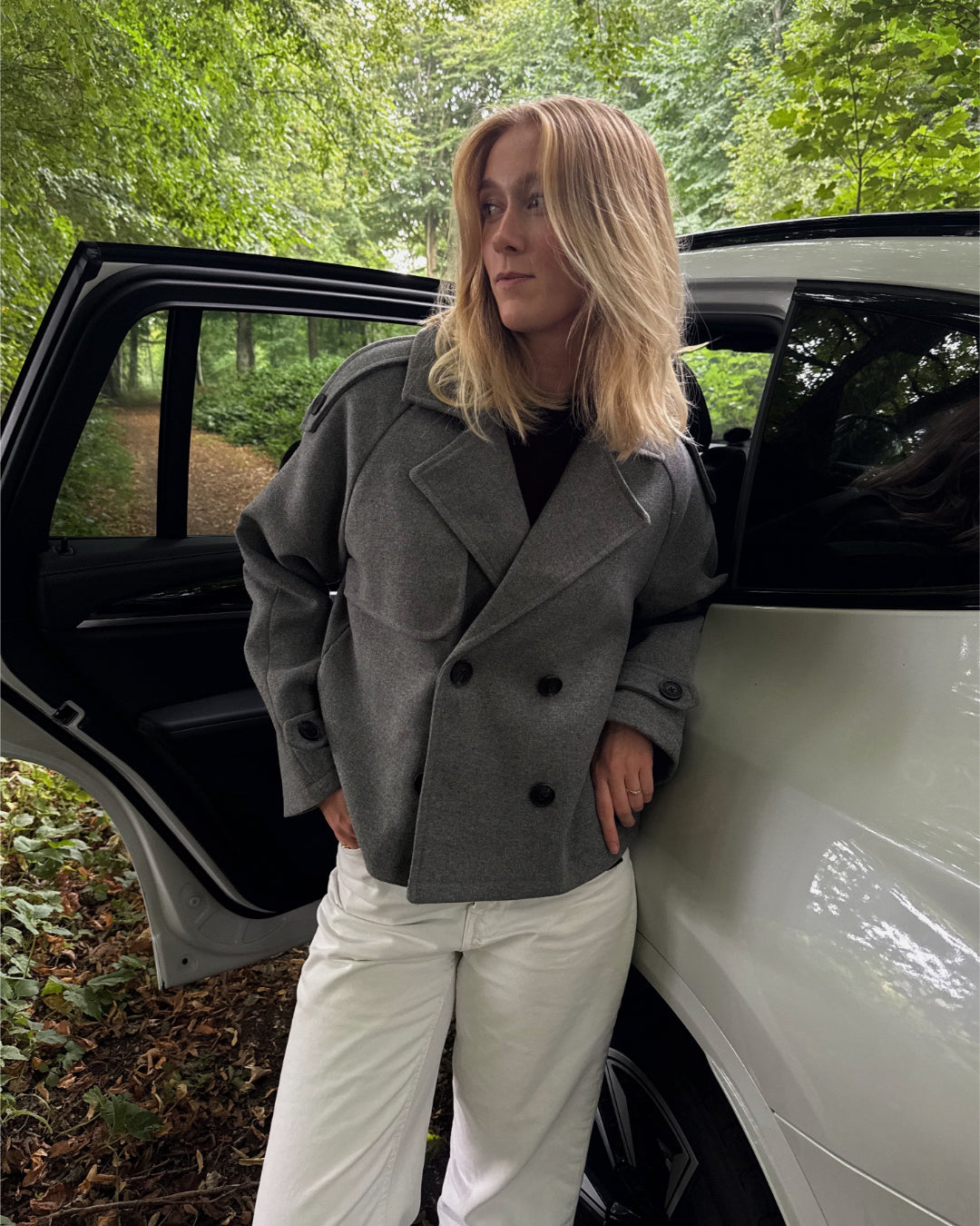 Modelfoto af pige i en grå Carlie jakke og hvide Nanna jeans. Alt er fra BySofieSønderby