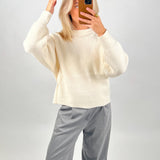 Person tager et billede. Iført en hvid sweater og grå bukser. De står foran en lys baggrund, og bruger en mobiltelefon med brunt etui til at tage billedet.